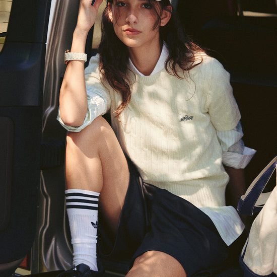 AROSRIS Cable Knit Lambswool Sweater in Cream Beige — outdoor lifestyle shot showing slim silhouette styled with white cap and bag