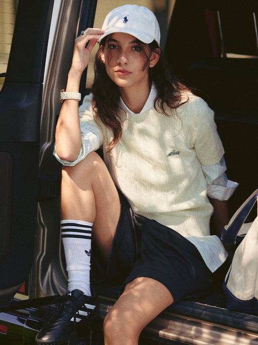 AROSRIS Cable Knit Lambswool Sweater in Cream Beige — outdoor lifestyle shot showing slim silhouette styled with white cap and bag