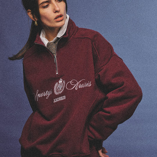 Arosris burgundy vintage-inspired campus half-zip sweatshirt with a custom crest embroidery, styled with biker shorts and retro sneakers for an effortless 90s sporty-chic aesthetic.
