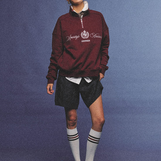 Arosris burgundy vintage-inspired campus half-zip sweatshirt with a custom crest embroidery, styled with biker shorts and retro sneakers for an effortless 90s sporty-chic aesthetic.