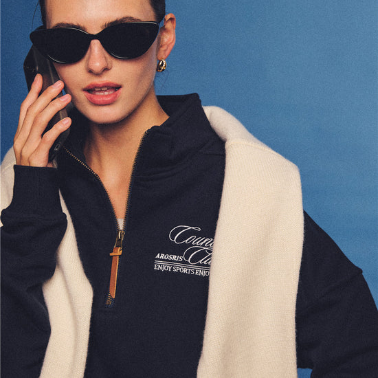 Arosris navy country club half-zip sweatshirt, expertly layered with a classic trench coat and vintage accessories for an effortless 90s sporty-rich aesthetic.
