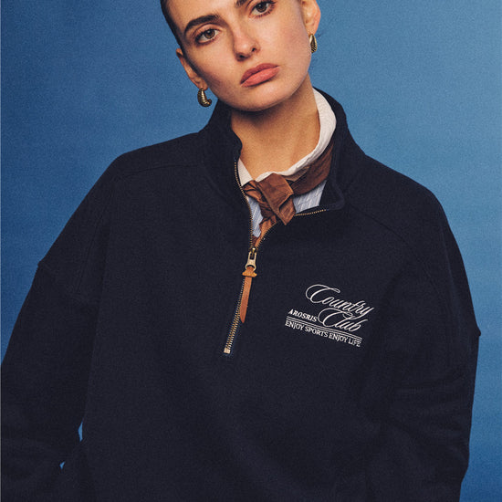 Arosris navy country club half-zip sweatshirt, expertly layered with a classic trench coat and vintage accessories for an effortless 90s sporty-rich aesthetic.