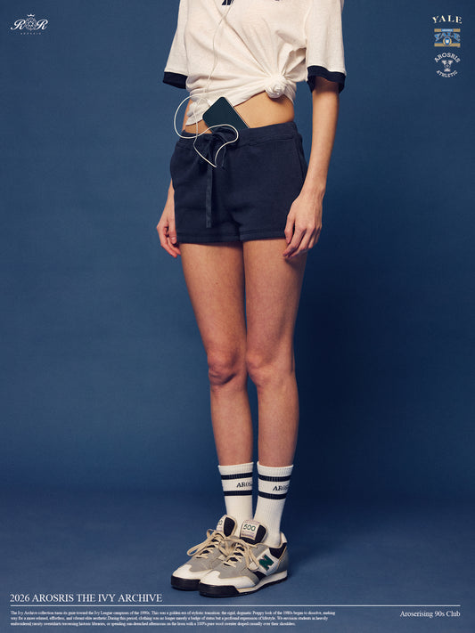 Arosris Ivy Archive high-rise varsity shorts featuring a 3-inch inseam and thick drawstring, elegantly styled on a model for an effortless 90s collegiate and sporty rich aesthetic.