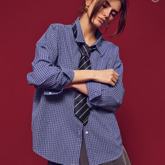 Arosris Ivy Archive oversized plaid shirt in blue, styled with a striped tie and grey pleated skirt for an effortless vintage 90s look.