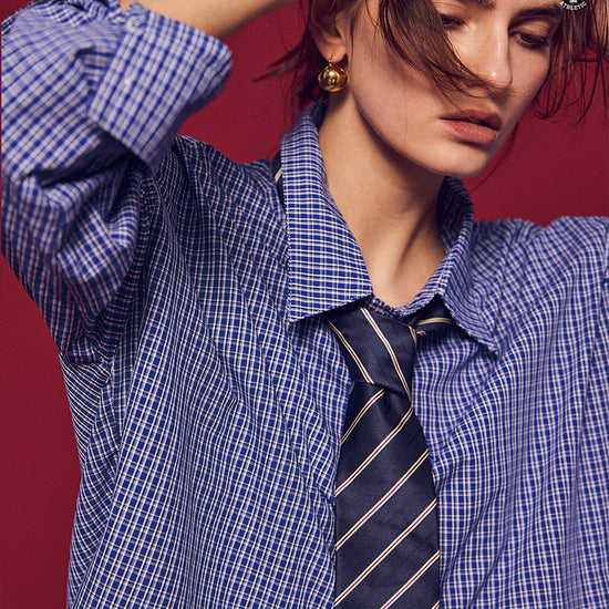 Arosris Ivy Archive oversized plaid shirt in blue, styled with a striped tie and grey pleated skirt for an effortless vintage 90s look.