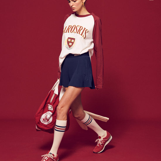 Arosris Ivy Archive collegiate raglan long sleeve in red, styled with a pleated skirt and a vintage tennis racket for an effortless 90s vintage varsity look.