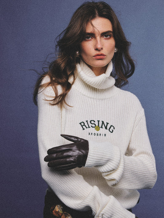 Arosris classic modern white ribbed wool blend turtleneck featuring a vintage 'RISING' floral embroidery, elegantly styled on a model as an effortless 90s preppy foundational layering piece.