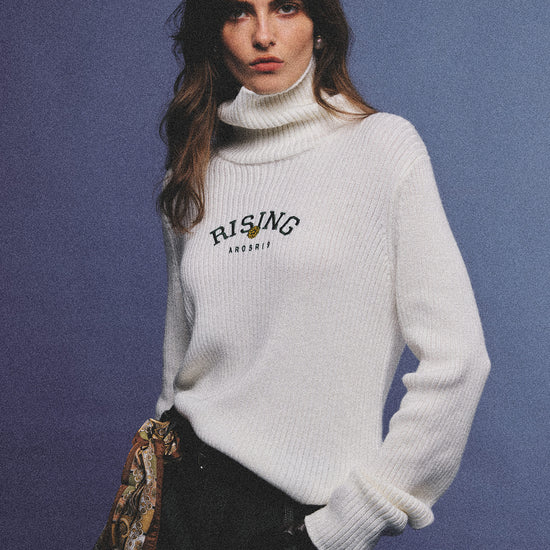 Arosris classic modern white ribbed wool blend turtleneck featuring a vintage 'RISING' floral embroidery, elegantly styled on a model as an effortless 90s preppy foundational layering piece.