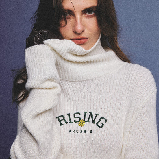 Arosris classic modern white ribbed wool blend turtleneck featuring a vintage 'RISING' floral embroidery, elegantly styled on a model as an effortless 90s preppy foundational layering piece.