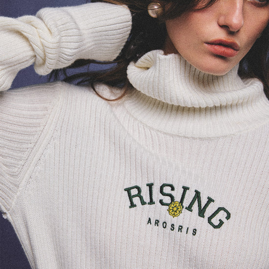 Arosris classic modern white ribbed wool blend turtleneck featuring a vintage 'RISING' floral embroidery, elegantly styled on a model as an effortless 90s preppy foundational layering piece.