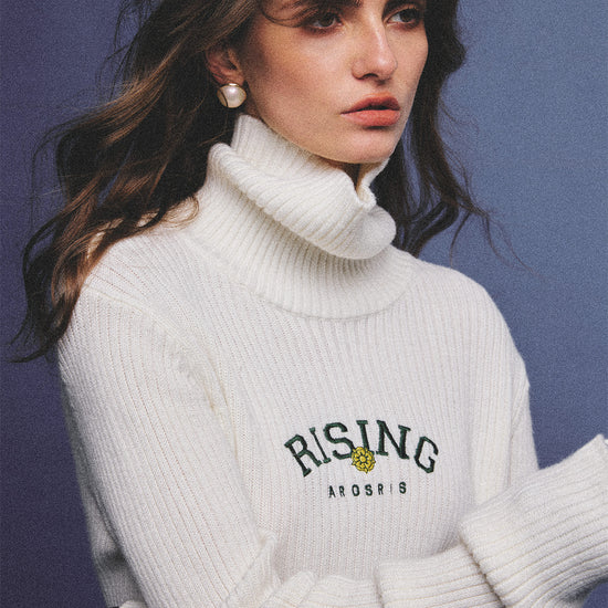 Arosris classic modern white ribbed wool blend turtleneck featuring a vintage 'RISING' floral embroidery, elegantly styled on a model as an effortless 90s preppy foundational layering piece.