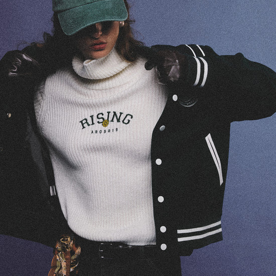Arosris classic modern white ribbed wool blend turtleneck featuring a vintage 'RISING' floral embroidery, elegantly styled on a model as an effortless 90s preppy foundational layering piece.