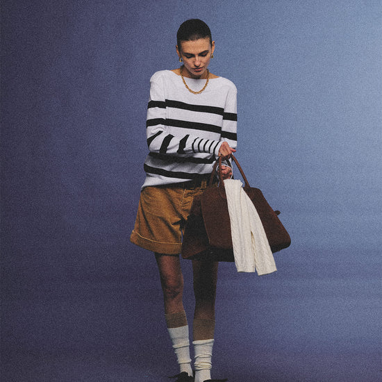 Arosris Riviera navy striped boat neck sweater elegantly styled on a model with corduroy shorts and vintage accessories, capturing an effortless 90s old money coastal resort aesthetic.