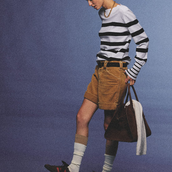 Arosris Riviera navy striped boat neck sweater elegantly styled on a model with corduroy shorts and vintage accessories, capturing an effortless 90s old money coastal resort aesthetic.
