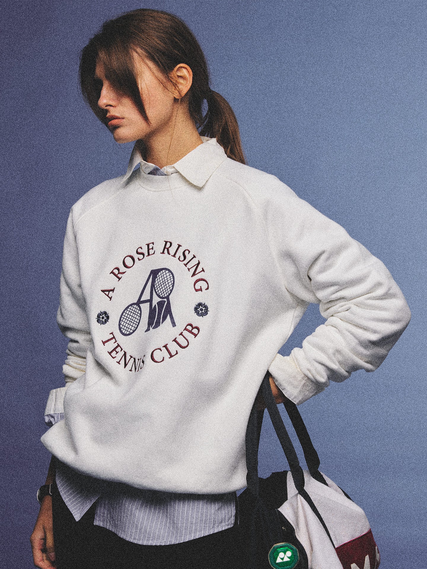 Arosris club white tennis club heritage sweatshirt with vintage crest graphic layered over a crisp collared shirt, elegantly styled on a model for an effortless 90s tenniscore and old money sporty rich aesthetic.