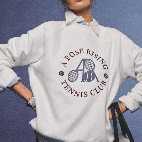 Arosris club white tennis club heritage sweatshirt with vintage crest graphic layered over a crisp collared shirt, elegantly styled on a model for an effortless 90s tenniscore and old money sporty rich aesthetic.