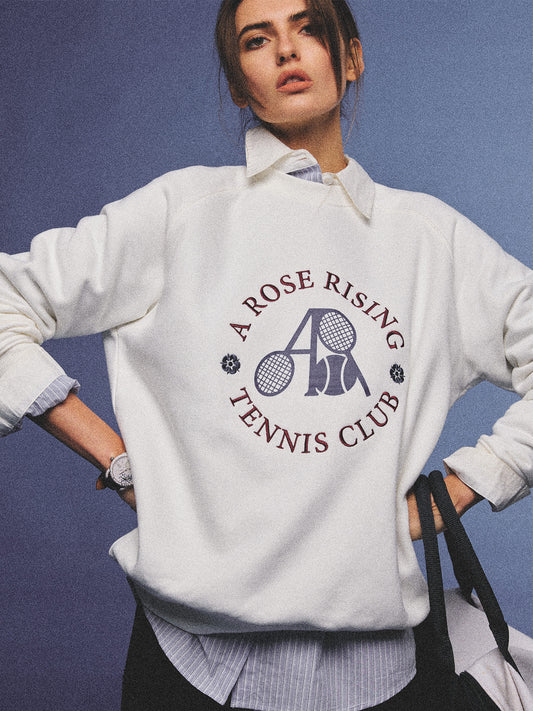 Arosris club white tennis club heritage sweatshirt with vintage crest graphic layered over a crisp collared shirt, elegantly styled on a model for an effortless 90s tenniscore and old money sporty rich aesthetic.