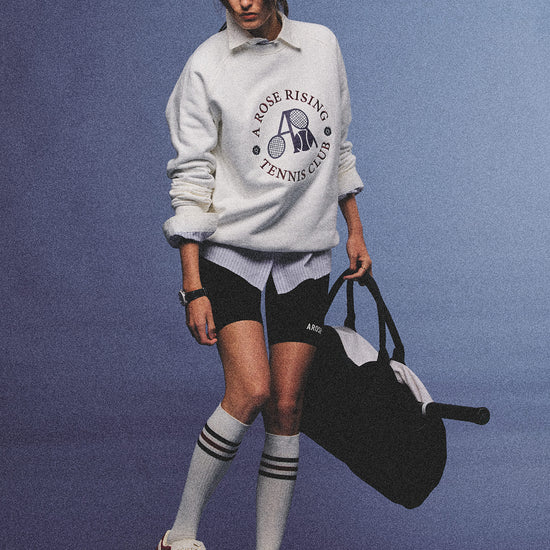 Arosris club white tennis club heritage sweatshirt with vintage crest graphic layered over a crisp collared shirt, elegantly styled on a model for an effortless 90s tenniscore and old money sporty rich aesthetic.