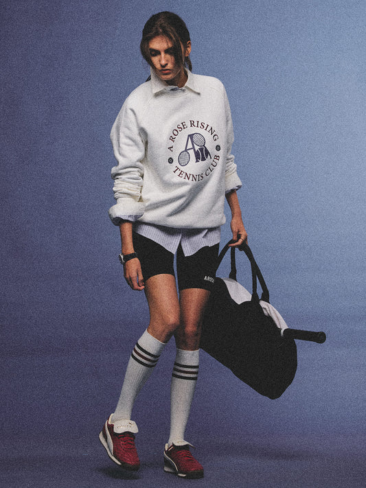 Arosris club white tennis club heritage sweatshirt with vintage crest graphic layered over a crisp collared shirt, elegantly styled on a model for an effortless 90s tenniscore and old money sporty rich aesthetic.
