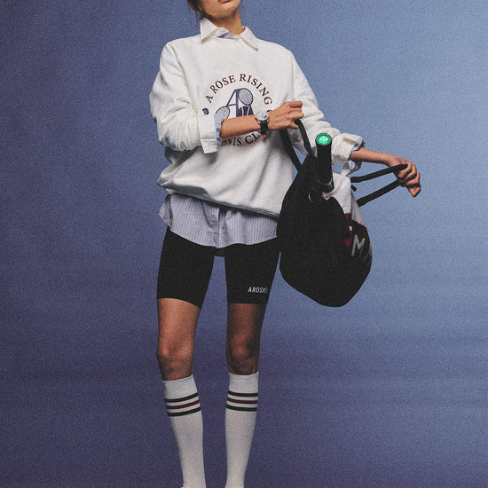 Arosris club white tennis club heritage sweatshirt with vintage crest graphic layered over a crisp collared shirt, elegantly styled on a model for an effortless 90s tenniscore and old money sporty rich aesthetic.