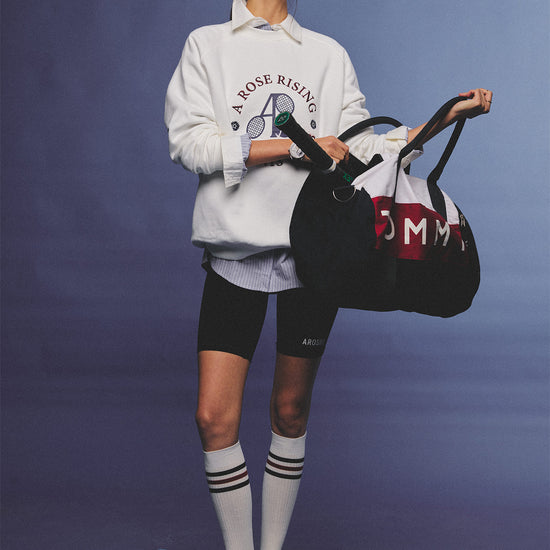 Arosris club white tennis club heritage sweatshirt with vintage crest graphic layered over a crisp collared shirt, elegantly styled on a model for an effortless 90s tenniscore and old money sporty rich aesthetic.