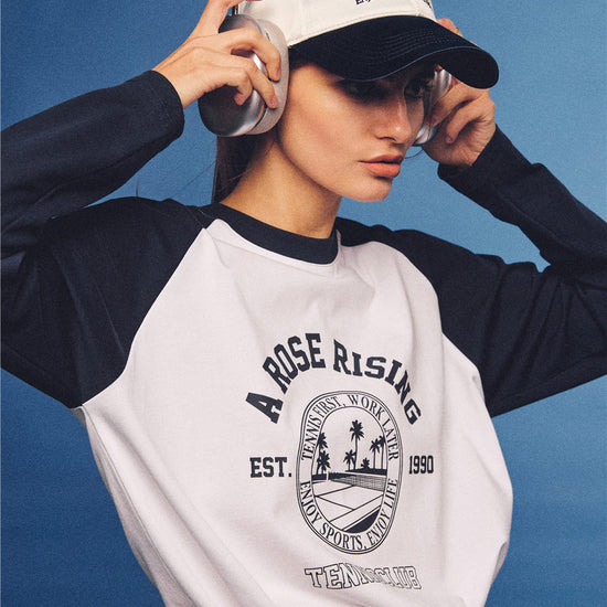 Arosris white and navy raglan long sleeve T-shirt, styled with a tennis skirt and cap for an effortless 90s vintage sporty-rich aesthetic.