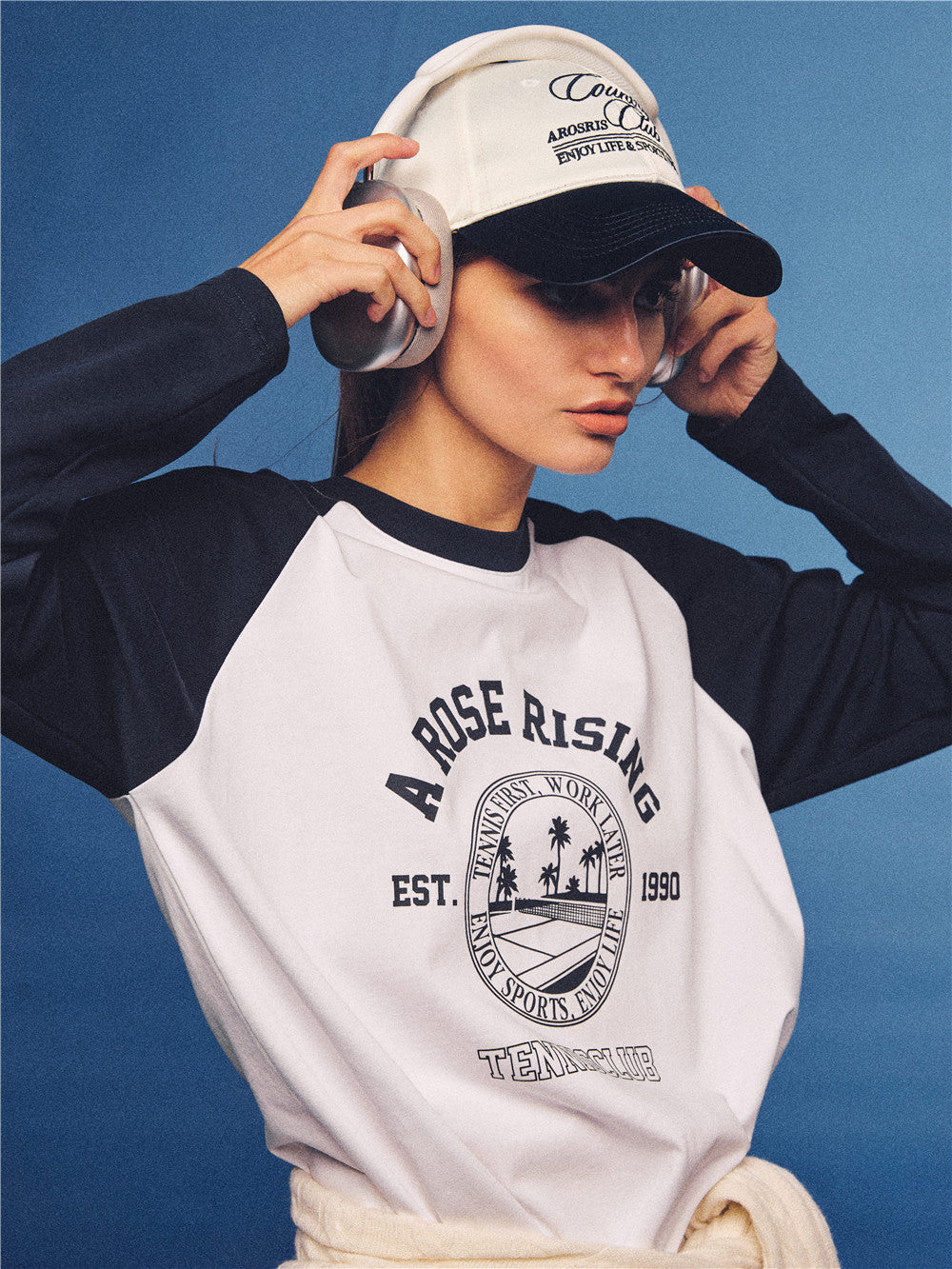 Arosris white and navy raglan long sleeve T-shirt, styled with a tennis skirt and cap for an effortless 90s vintage sporty-rich aesthetic.