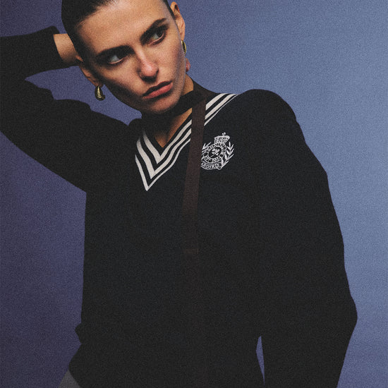 Arosris deep sapphire tennis club v-neck sweater crafted from 100% premium sheep wool, featuring contrast stripes and a vintage crest, elegantly styled on a model for an effortless 90s preppy old money and tenniscore aesthetic.