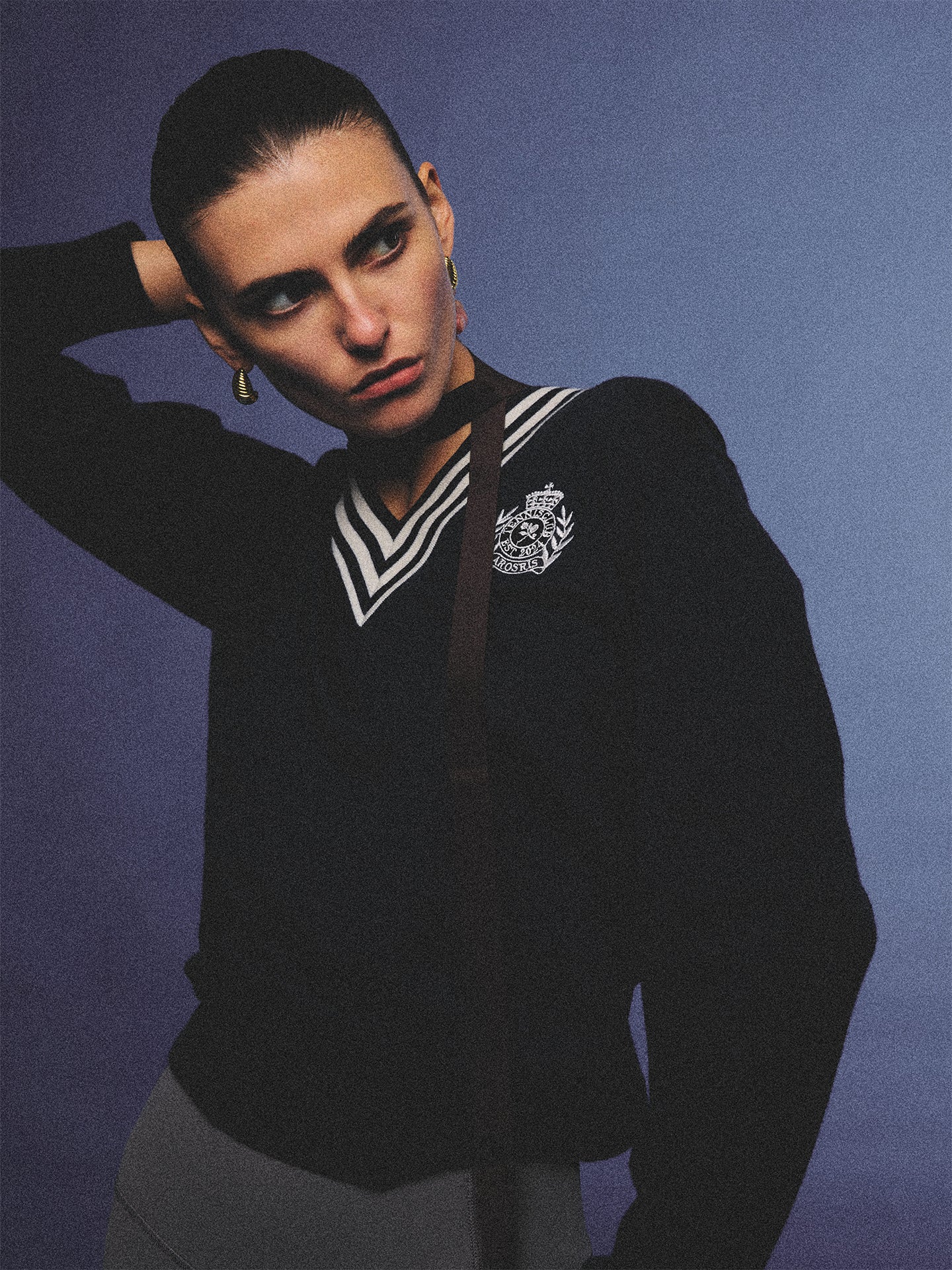 Arosris deep sapphire tennis club v-neck sweater crafted from 100% premium sheep wool, featuring contrast stripes and a vintage crest, elegantly styled on a model for an effortless 90s preppy old money and tenniscore aesthetic.