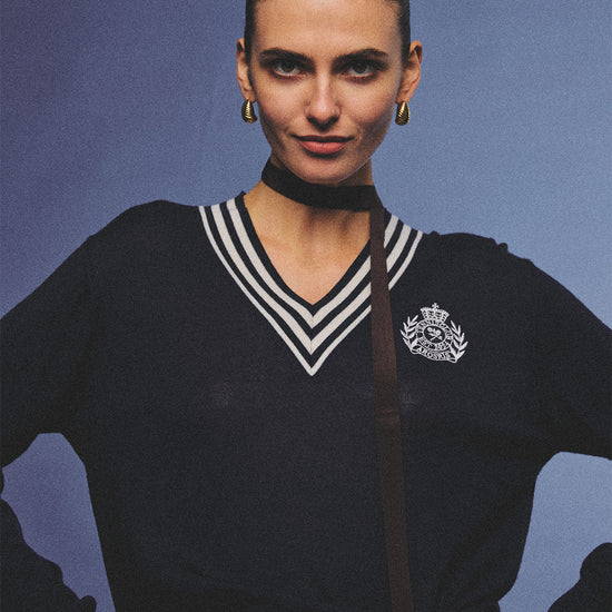 Arosris deep sapphire tennis club v-neck sweater crafted from 100% premium sheep wool, featuring contrast stripes and a vintage crest, elegantly styled on a model for an effortless 90s preppy old money and tenniscore aesthetic.