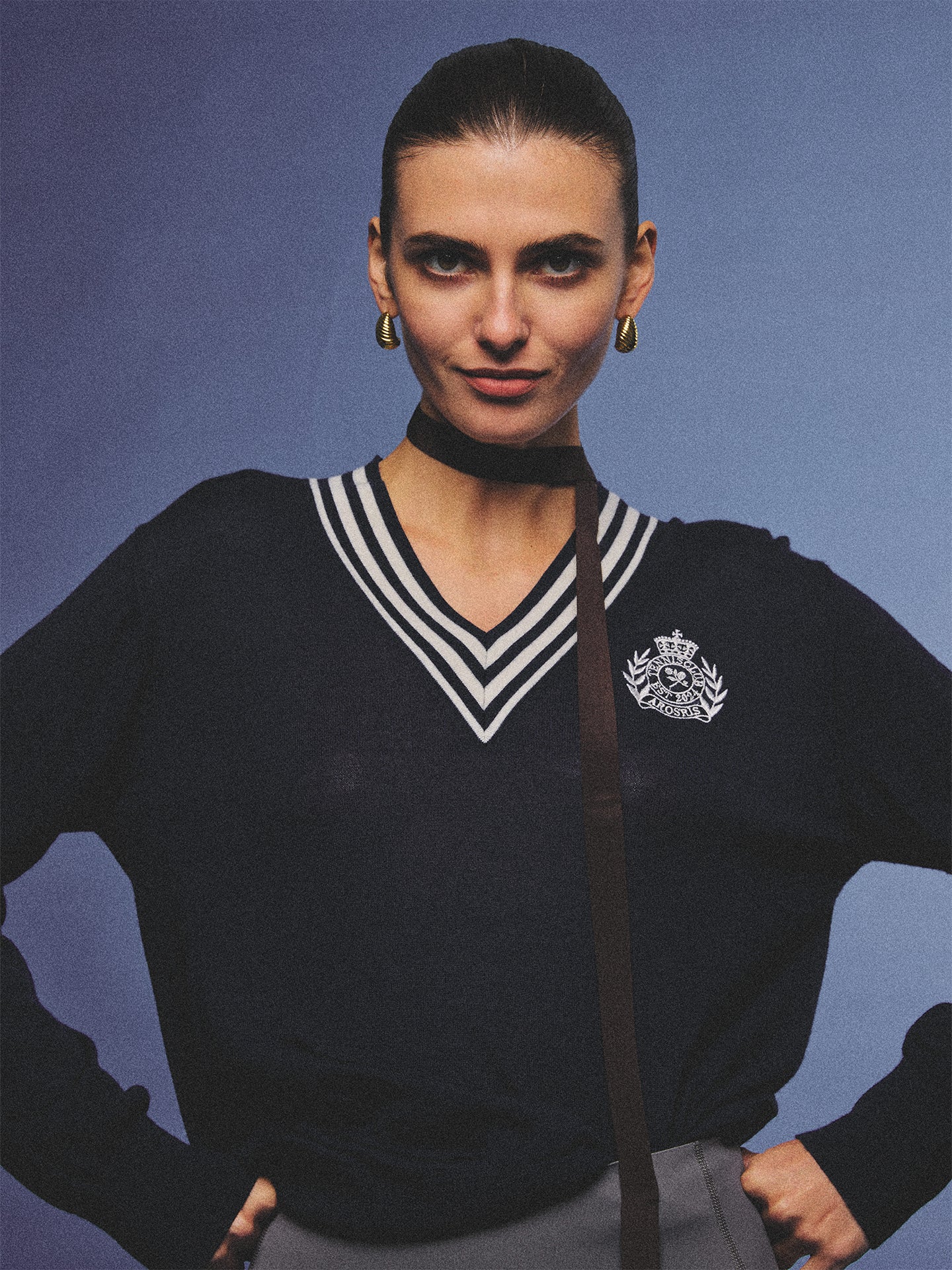 Arosris deep sapphire tennis club v-neck sweater crafted from 100% premium sheep wool, featuring contrast stripes and a vintage crest, elegantly styled on a model for an effortless 90s preppy old money and tenniscore aesthetic.