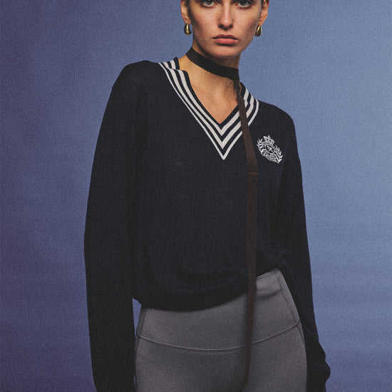 Arosris deep sapphire tennis club v-neck sweater crafted from 100% premium sheep wool, featuring contrast stripes and a vintage crest, elegantly styled on a model for an effortless 90s preppy old money and tenniscore aesthetic.