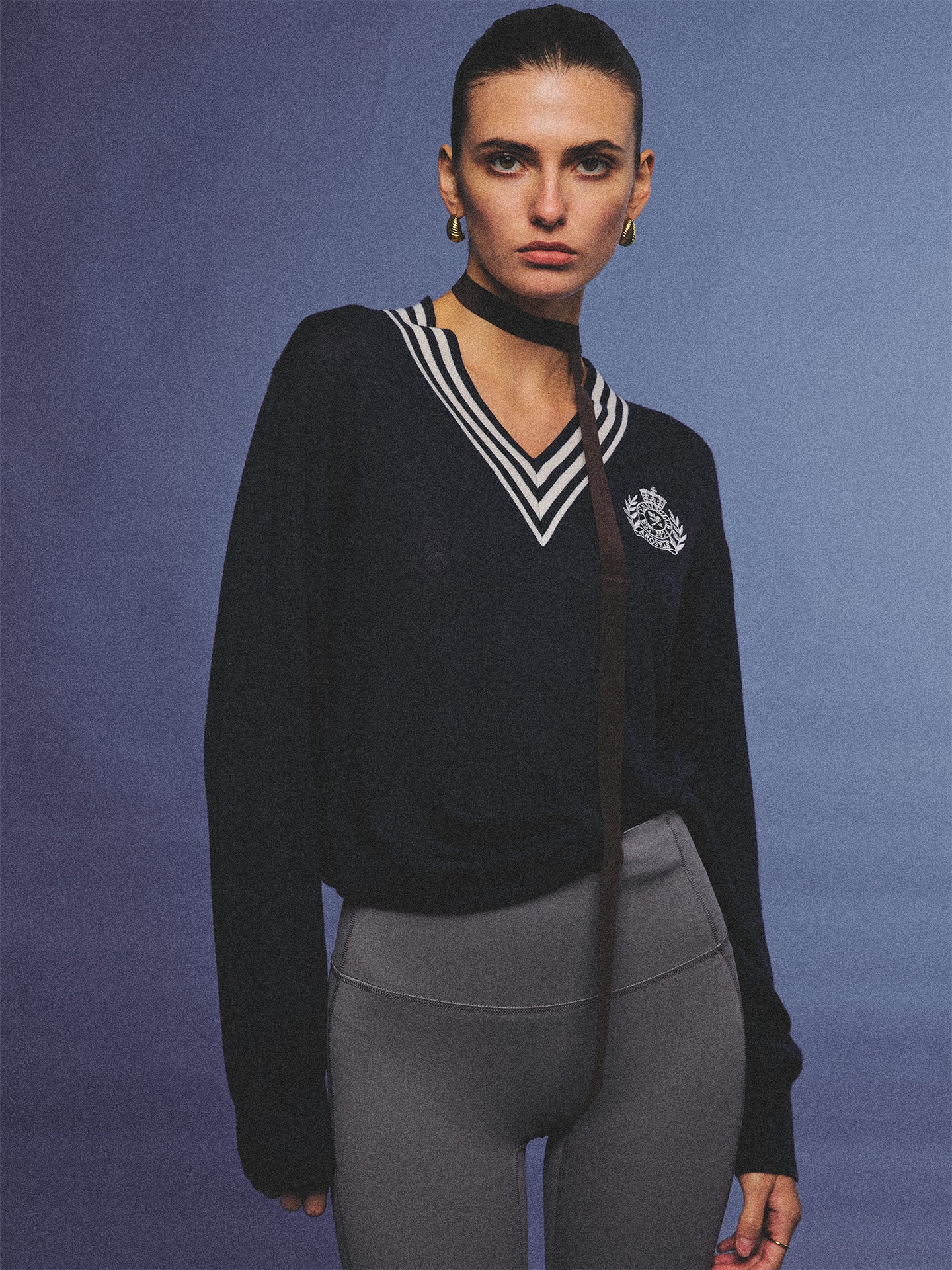Arosris deep sapphire tennis club v-neck sweater crafted from 100% premium sheep wool, featuring contrast stripes and a vintage crest, elegantly styled on a model for an effortless 90s preppy old money and tenniscore aesthetic.