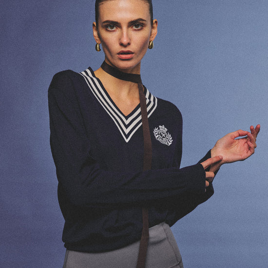 Arosris deep sapphire tennis club v-neck sweater crafted from 100% premium sheep wool, featuring contrast stripes and a vintage crest, elegantly styled on a model for an effortless 90s preppy old money and tenniscore aesthetic.