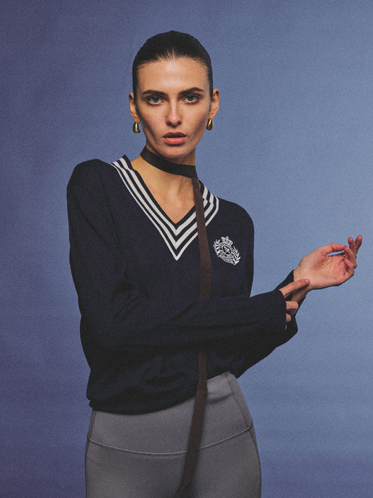 Arosris deep sapphire tennis club v-neck sweater crafted from 100% premium sheep wool, featuring contrast stripes and a vintage crest, elegantly styled on a model for an effortless 90s preppy old money and tenniscore aesthetic.
